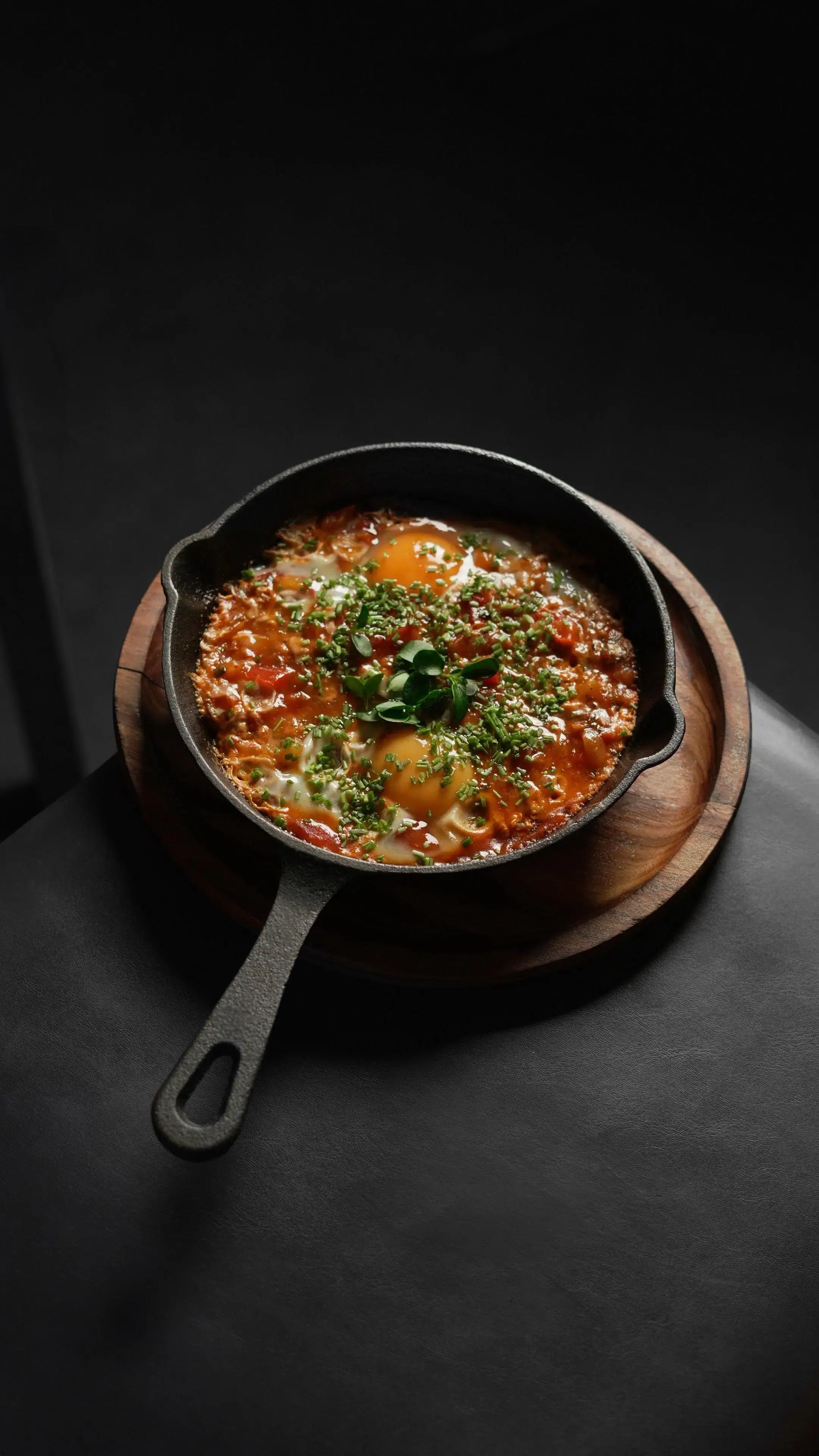 Eine gusseiserne Pfanne mit buntem Shakshuka und frischen Kräutern auf Holzbrett