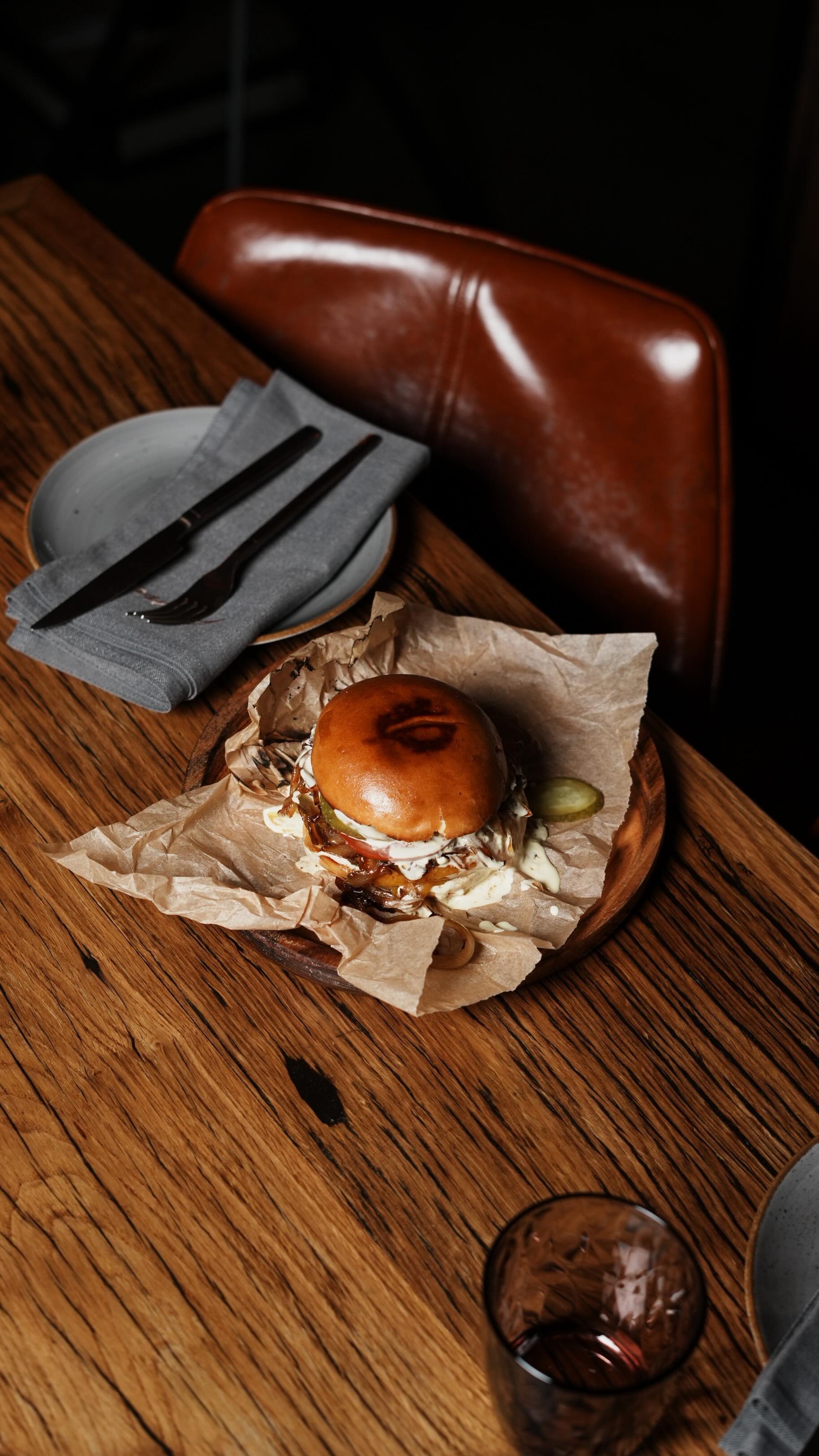 Ein Burger mit glänzendem Brötchen liegt appetitlich auf braunem Papier auf einem Holztisch